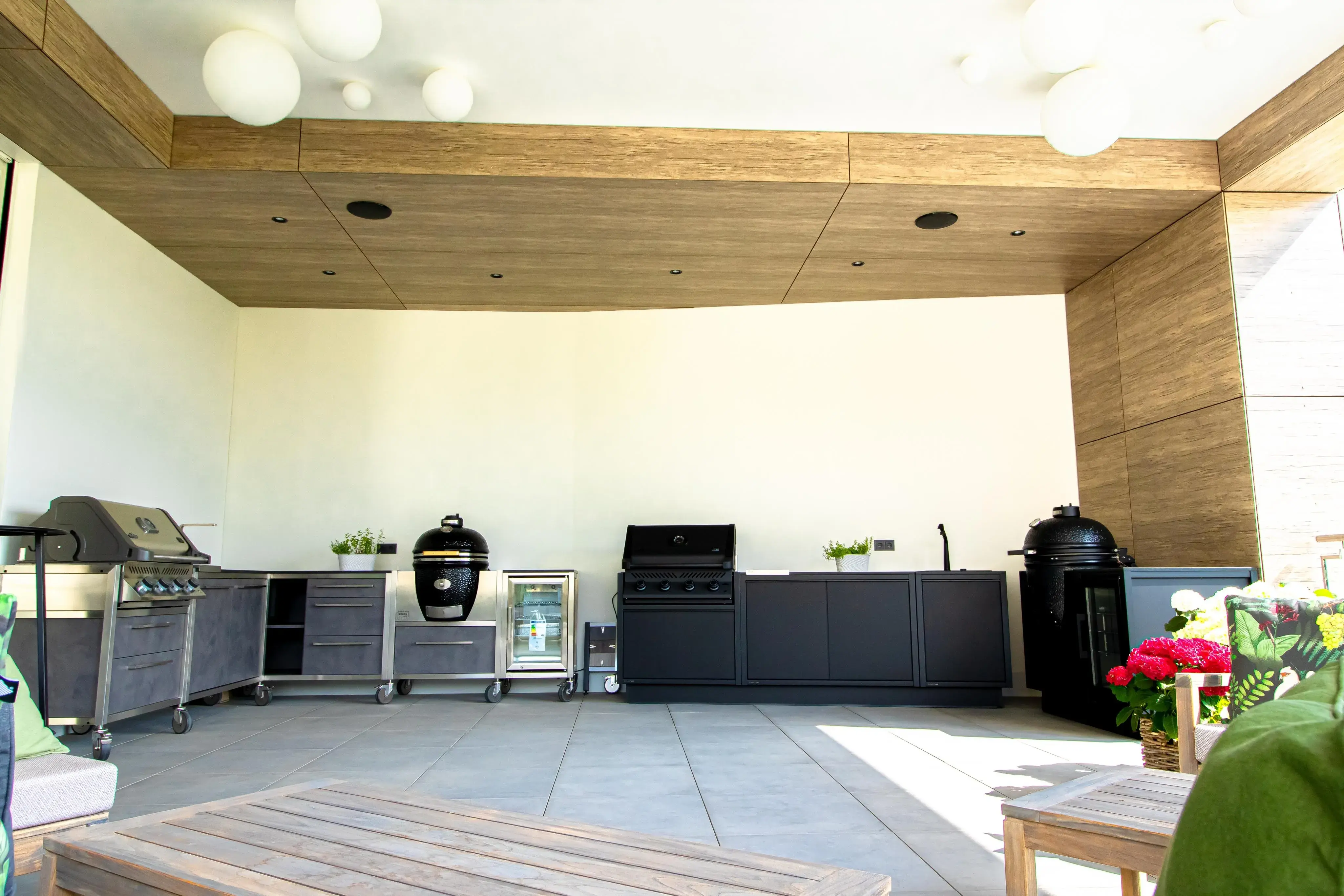 Moderne Outdoor-Küche mit Grillgeräten, Holzdecke und großen Fliesen.