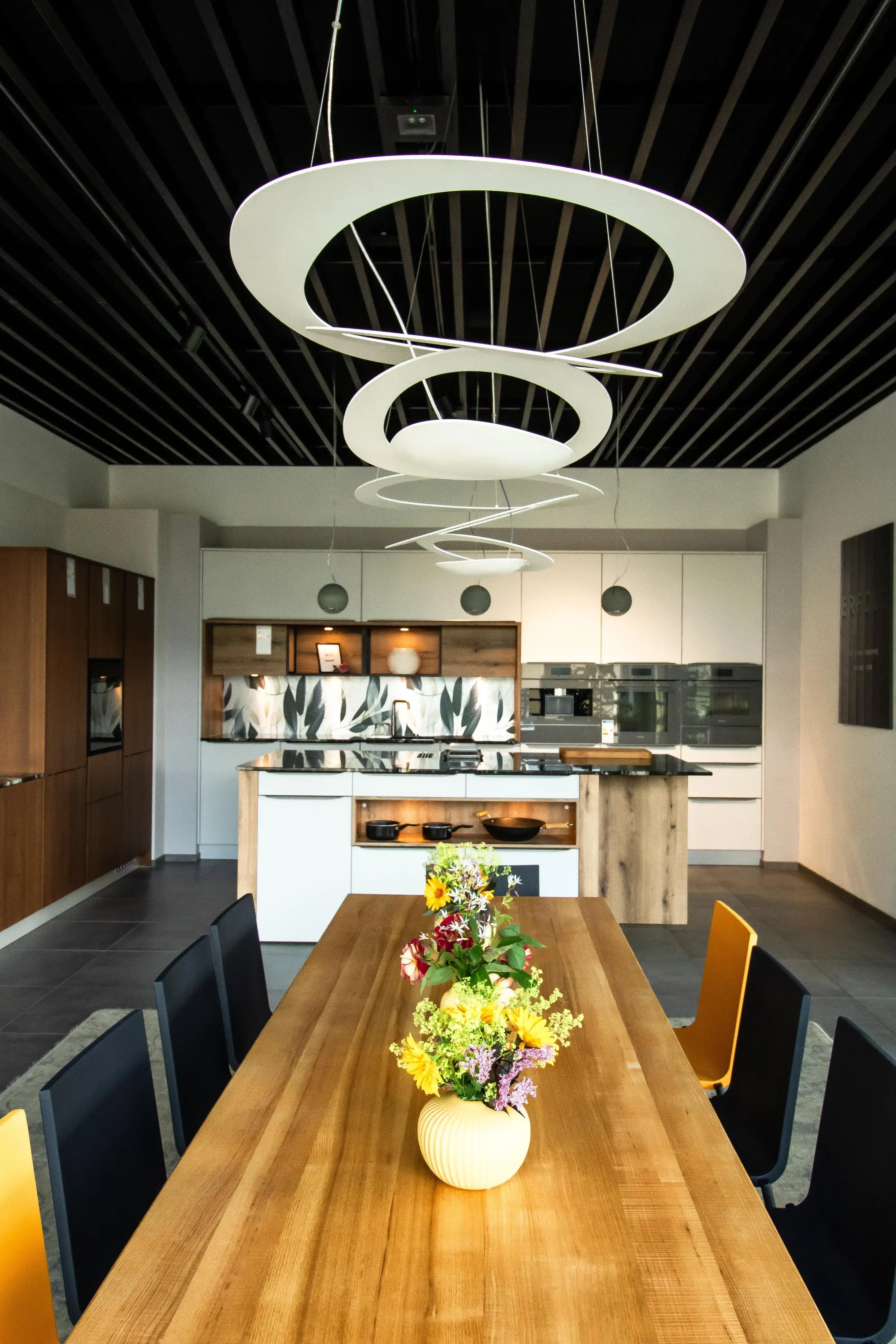 Moderne Küche mit Holztisch, Blumenstrauß und auffälligen Deckenleuchten.