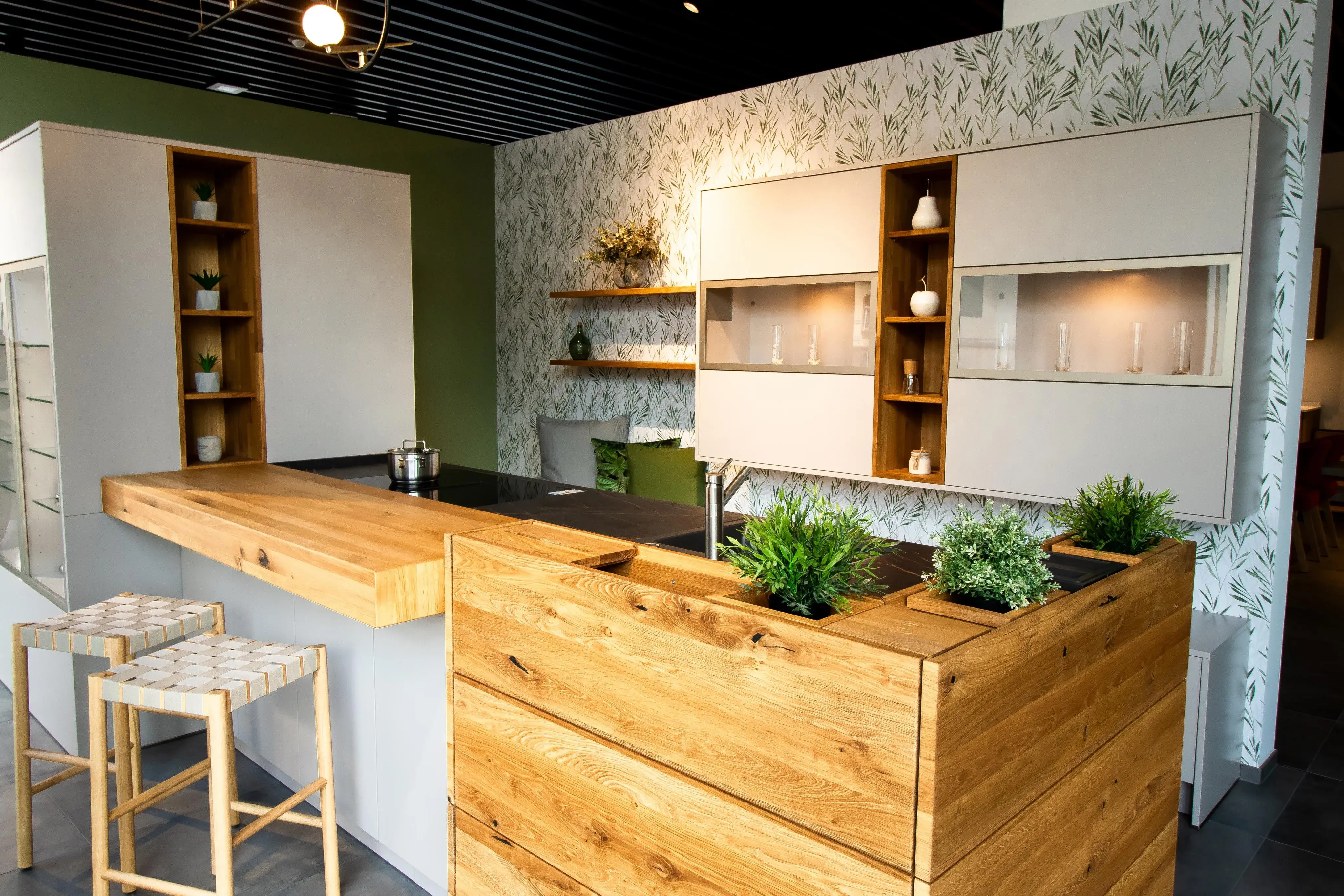 Moderne Küche mit Holzelementen, grünen Pflanzen und hellen Hockern.