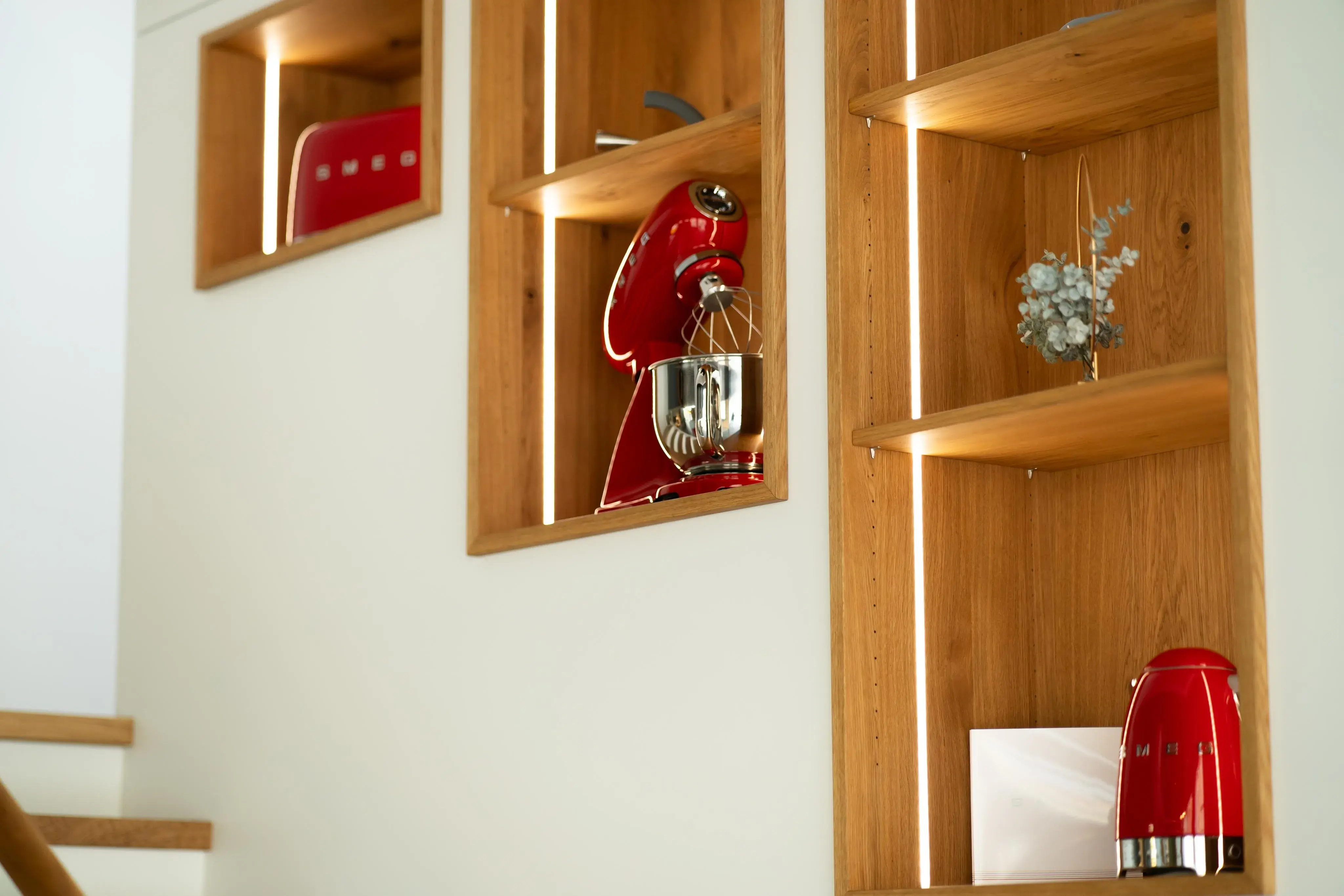 Holzregale in der Wand mit roten Küchengeräten und einer kleinen Pflanze.